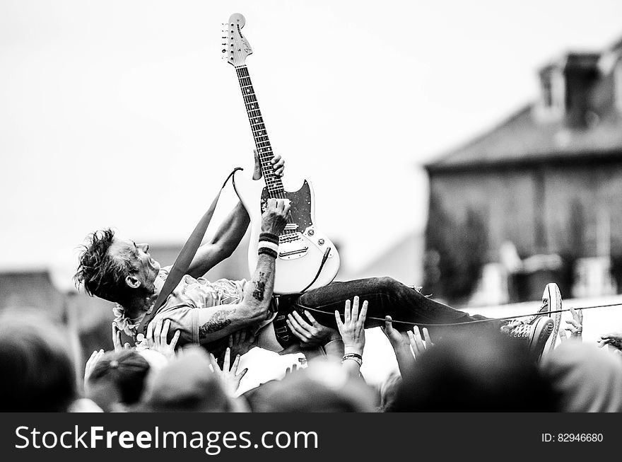 Gray Scale Photo of Man Lifted by People Holding Stratocaster Guitar