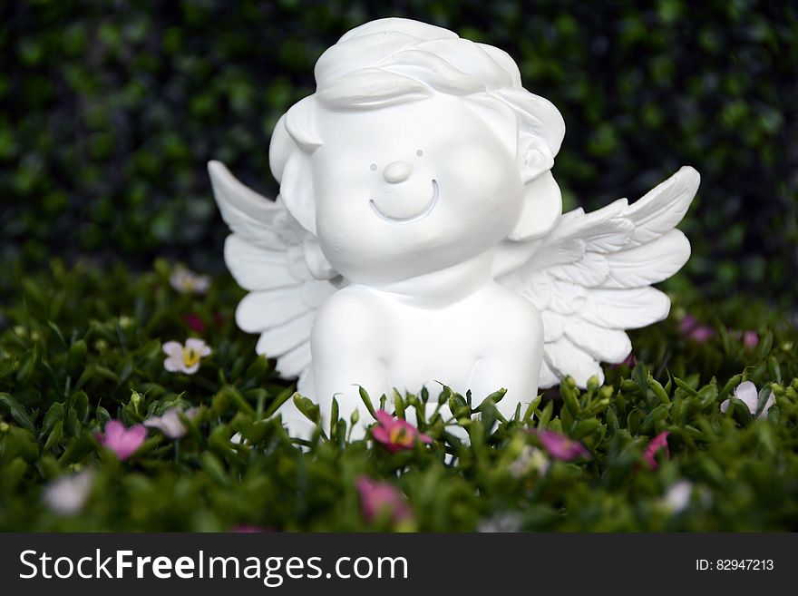 White Angel Ceramic Figurine on Green Grass With White and Purple Flower