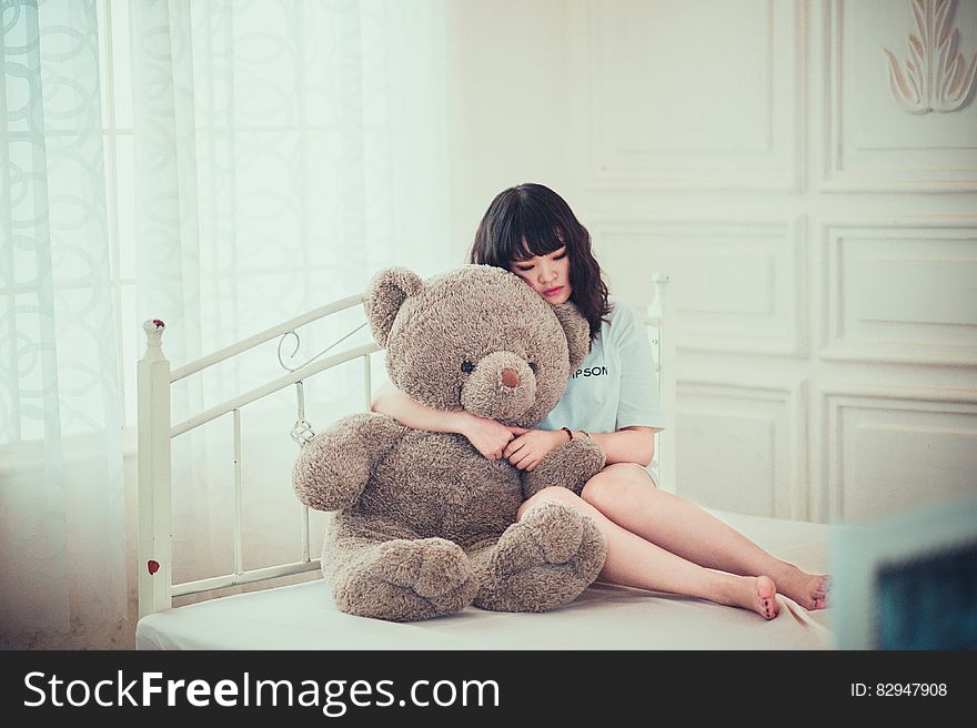 Portrait of beautiful Asian woman hugging teddy bear sitting on bed inside bedroom. Portrait of beautiful Asian woman hugging teddy bear sitting on bed inside bedroom.