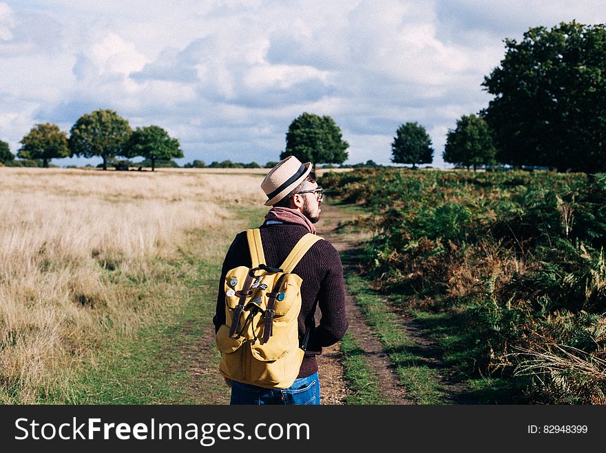 Man With Backpack Walking on Pathway Between Field at Daytime