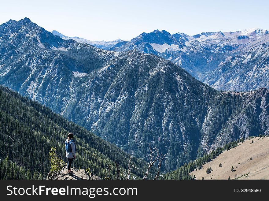 Hiker on mountain peak looking over valley forest.