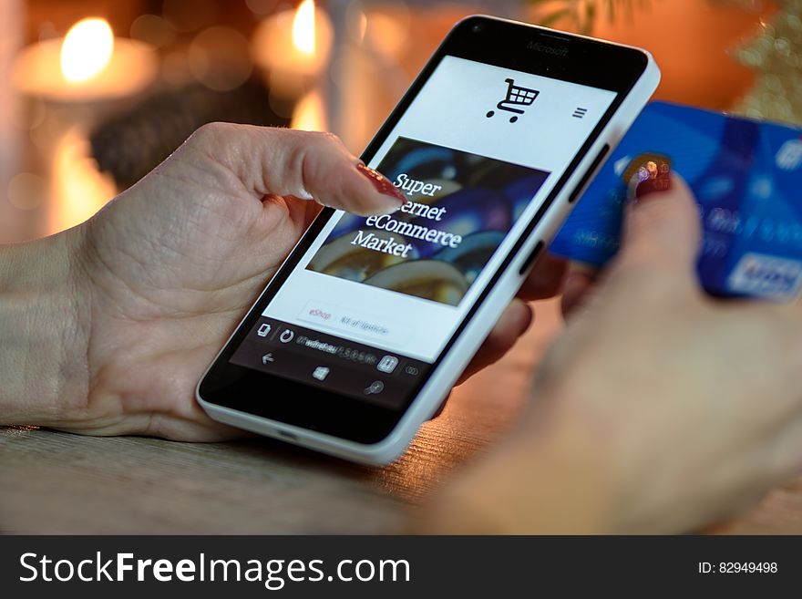 Person Using Black And White Smartphone and Holding Blue Card