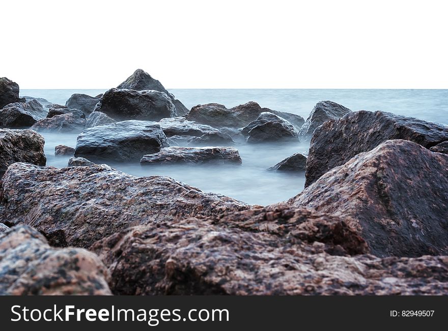 Sea and incoming tide on large granite rocks with mist rising from the water, gray dull background sky. Sea and incoming tide on large granite rocks with mist rising from the water, gray dull background sky.
