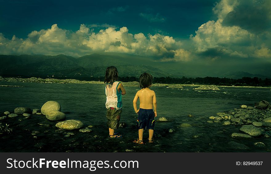 Child in White Tank Top Beside Child in Black Shorts Near Sea during Daytime