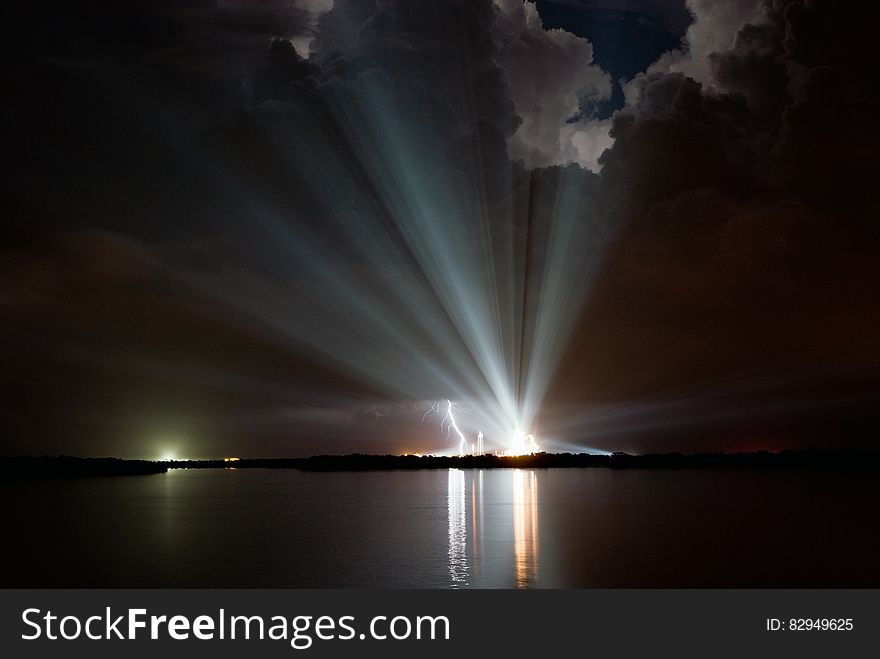 Lightening strike next to bright spotlight along waterfront in night skies. Lightening strike next to bright spotlight along waterfront in night skies.