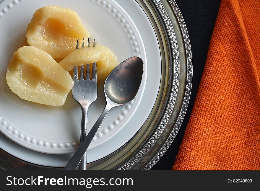 Overhead view of pear halves on white china plate with fork and spoon on chargers with orange napkin. Overhead view of pear halves on white china plate with fork and spoon on chargers with orange napkin.