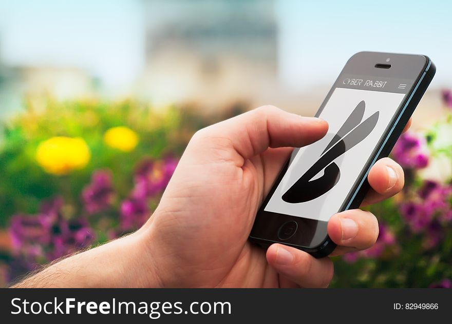 Hand holding smartphone with Cyber Rabbit logo outdoor in flower garden. Hand holding smartphone with Cyber Rabbit logo outdoor in flower garden.