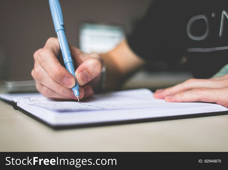 Person Holding Blue Ballpoint Pen Writing in Notebook