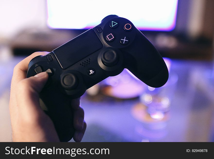 Close up of hand holding gaming console in front of television set inside home.