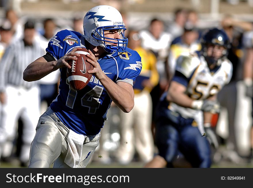 American football player holding ball while running during game. American football player holding ball while running during game.