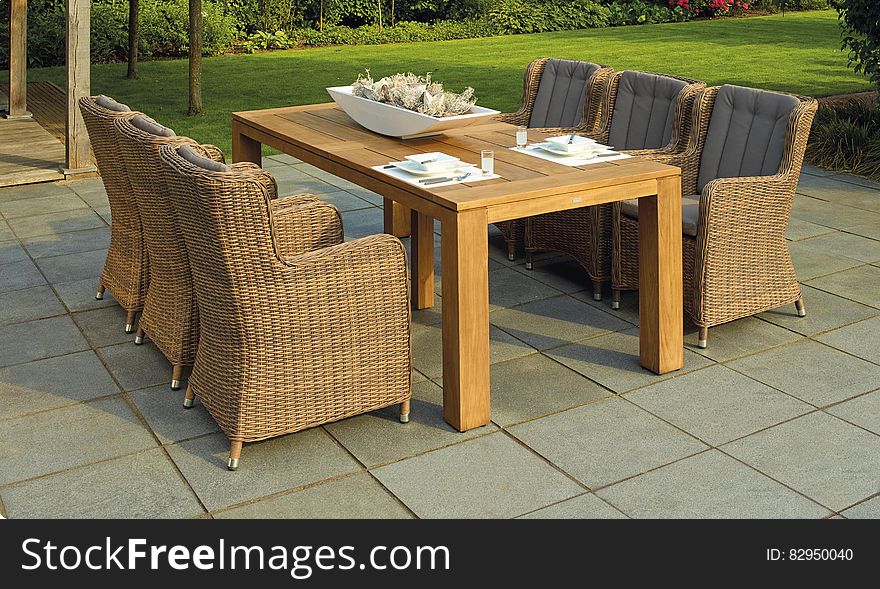 Wicker chairs and wooden patio table on garden deck on sunny day. Wicker chairs and wooden patio table on garden deck on sunny day.