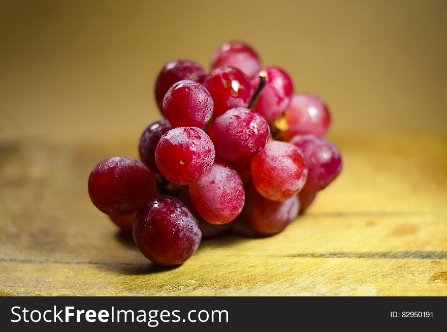 A bunch of fresh red grapes glistening in the light closeup with selective focus and a yellow wooden background.