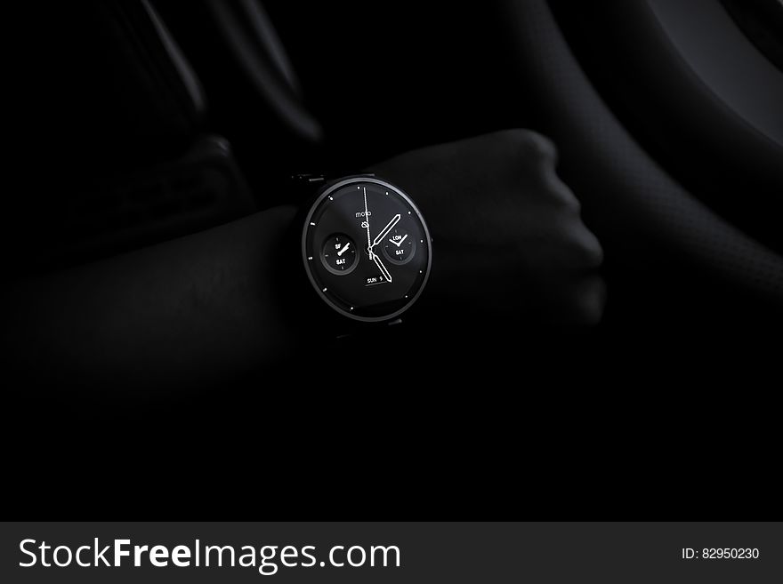 Stylish modern wristwatch in front of shadowed hand on black background.
