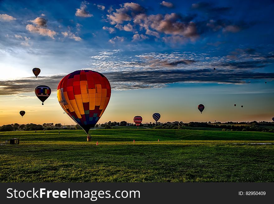 Colorful group of hot air balloons floating over countryside field at sunset with picturesque cloudscape. Colorful group of hot air balloons floating over countryside field at sunset with picturesque cloudscape.