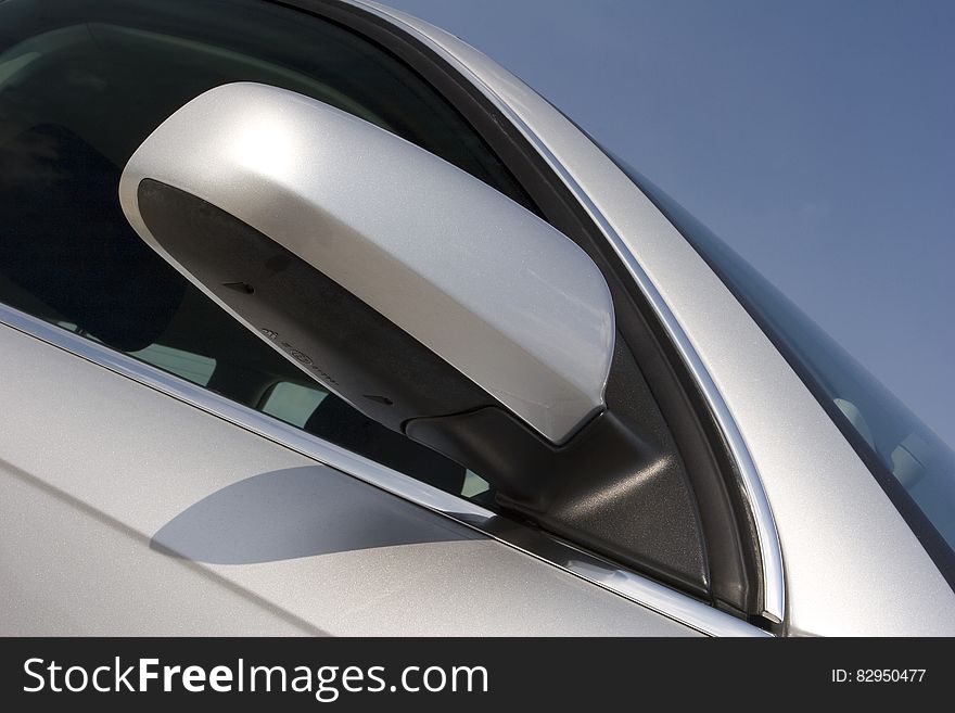 Front of silver luxury car door and side mirror against blue skies. Front of silver luxury car door and side mirror against blue skies.