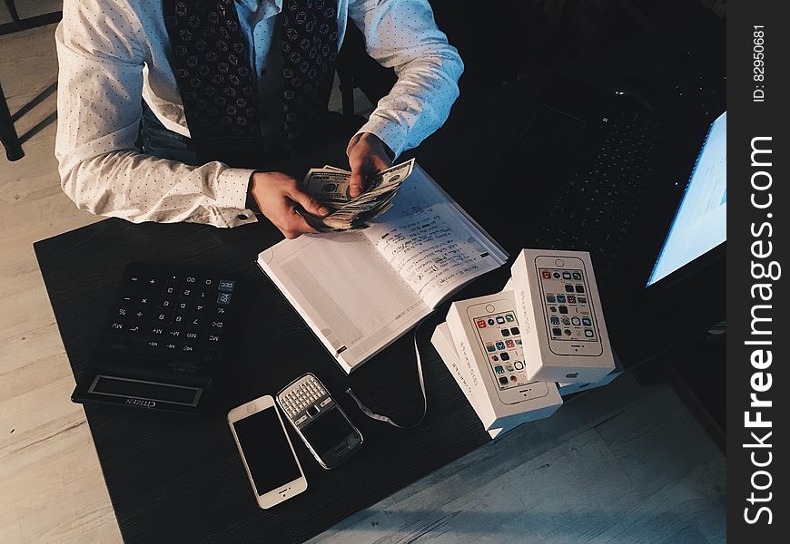 Person Counting Money With Smartphones in Front on Desk