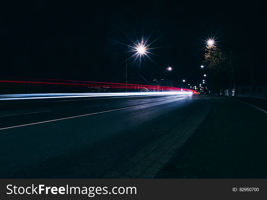 Highway with bright white car headlights approaching and another vehicle with its rear lights receding and with two bright overhead lights illuminating an otherwise black night. Highway with bright white car headlights approaching and another vehicle with its rear lights receding and with two bright overhead lights illuminating an otherwise black night.