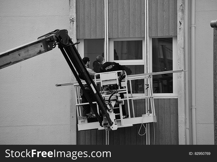 Maintenance workers in lift working on outdoor urban window in black and white.