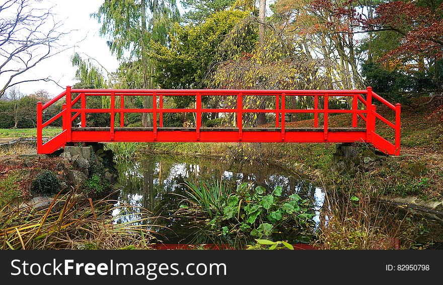 Red wooden bridge over creek in garden or park. Red wooden bridge over creek in garden or park.