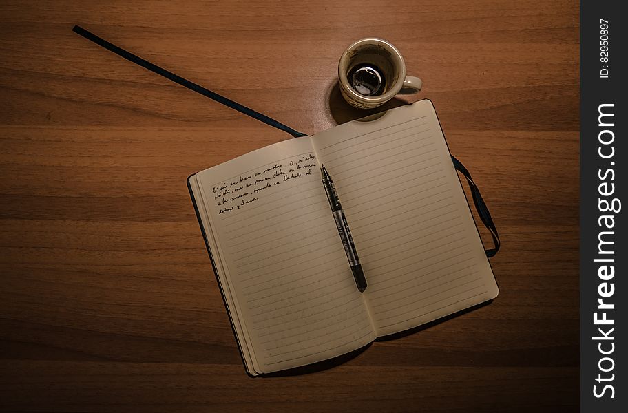 Pen on Notebook Beside a Teacup on Brown Wooden Plank