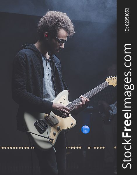 Guitarist with punk rock band playing electric guitar on stage, black background.