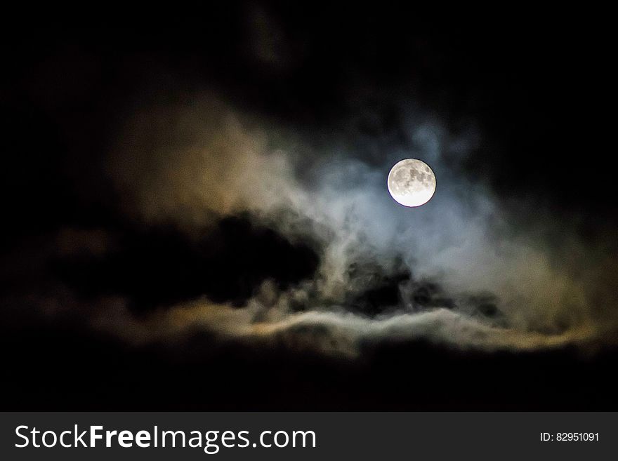 A full moon behind clouds in the night sky.