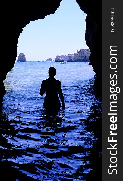 Silhouette of Woman at Blue Sea Inside Black Cave during Daytime