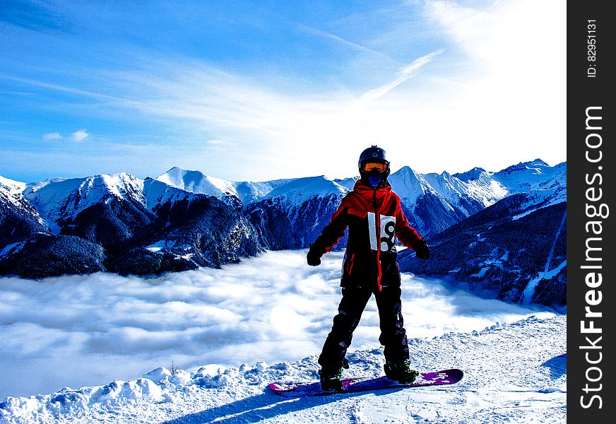 A snowboarder standing on a mountain peak, a spectacular view of the mountain range behind him.