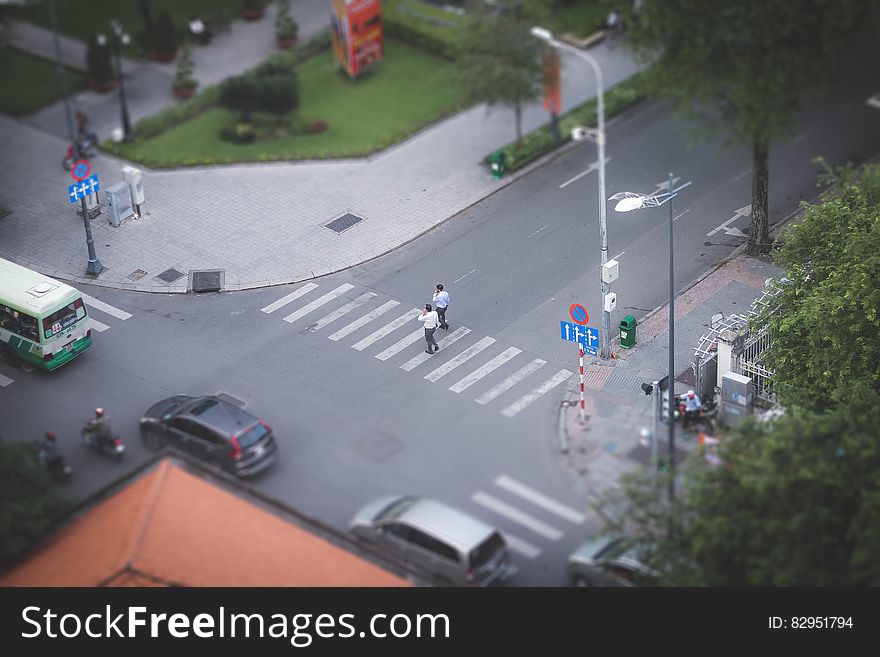 Aerial view of pedestrians in crosswalk at city intersection with traffic on sunny day.