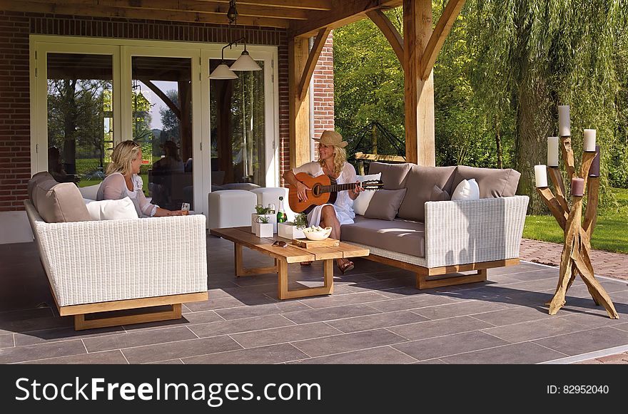 Women sitting on outdoor patio furniture playing guitar on sunny day. Women sitting on outdoor patio furniture playing guitar on sunny day.