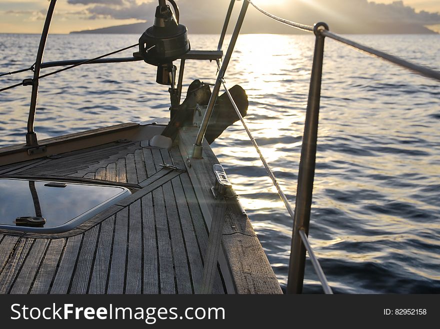 Bow of wooden boat sailing on waters with island on horizon at sunset. Bow of wooden boat sailing on waters with island on horizon at sunset.