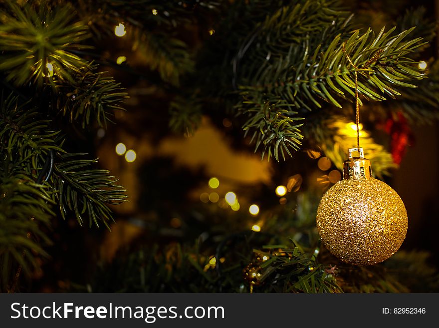 Gold ball ornament hanging on Christmas tree with lights. Gold ball ornament hanging on Christmas tree with lights.