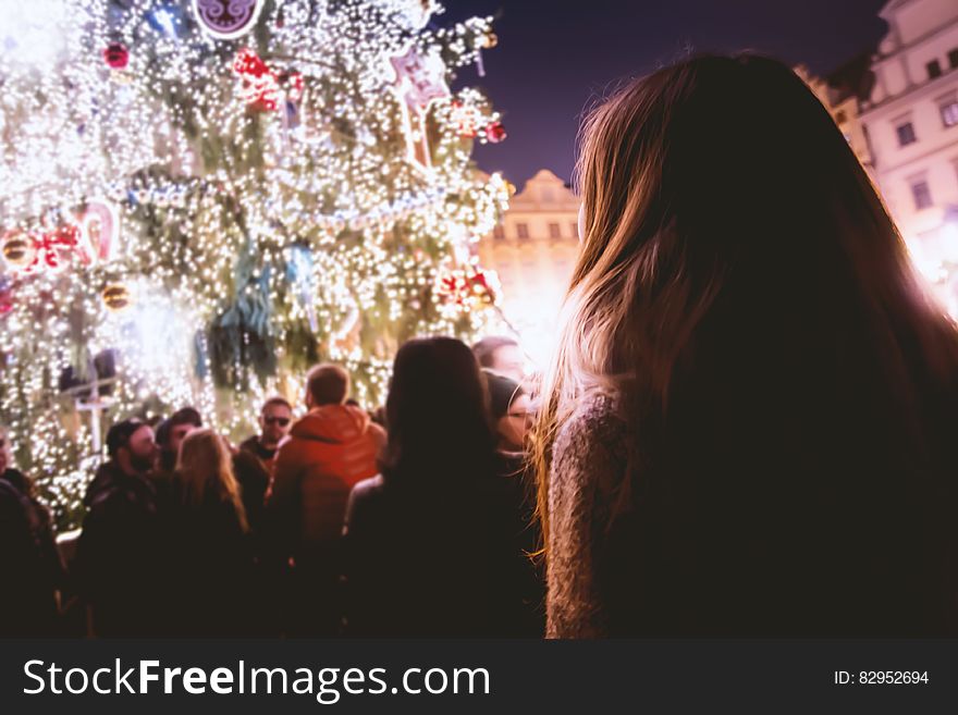 People at Christmas festival around lit tree at night.