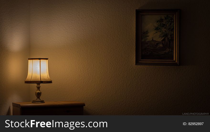 Lamp illuminated in dark room with table and painting. Lamp illuminated in dark room with table and painting.