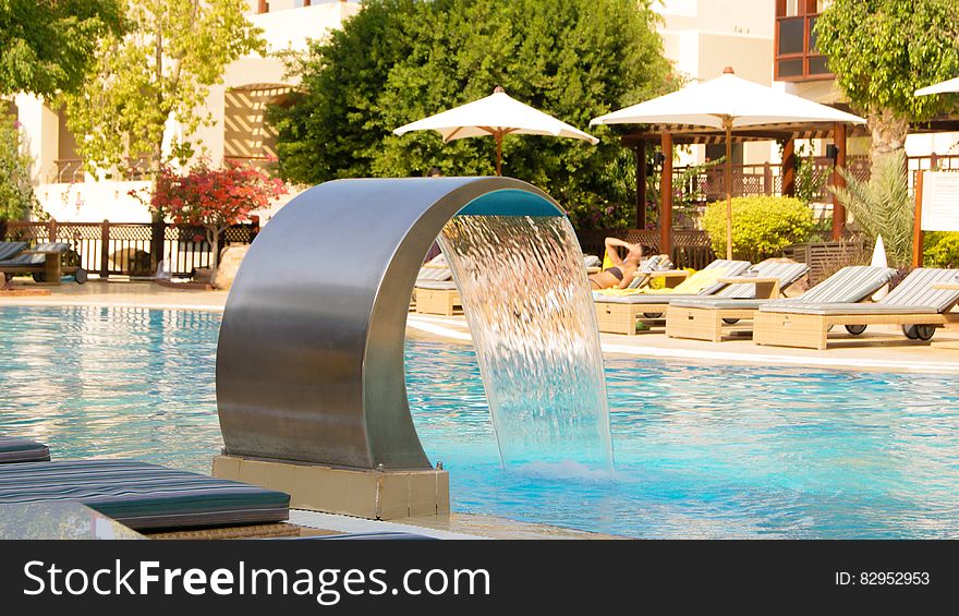 Water fountain cascading into hotel swimming pool with sunbeds and parasols in background. Water fountain cascading into hotel swimming pool with sunbeds and parasols in background.