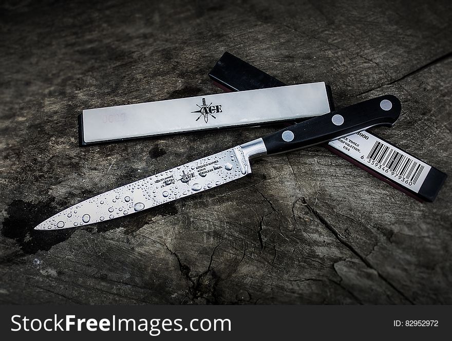 Drops of water on kitchen knife next to case on dark wooden background.