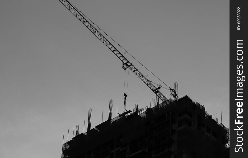 Crane on rooftop of modern building under construction silhouetted in black and white. Crane on rooftop of modern building under construction silhouetted in black and white.