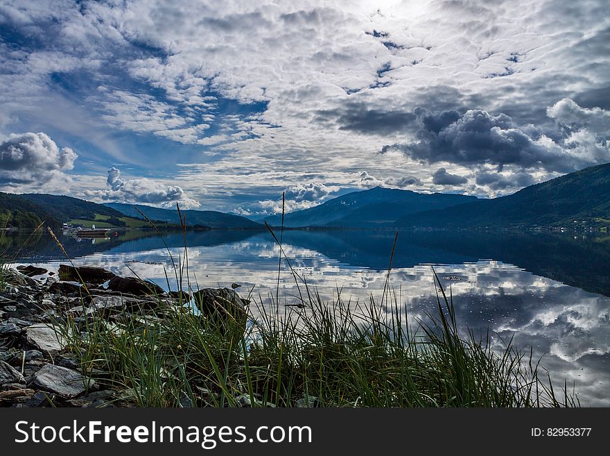 Clouds and blue skies reflecting in alpine lake in foothills of mountain range on sunny day. Clouds and blue skies reflecting in alpine lake in foothills of mountain range on sunny day.