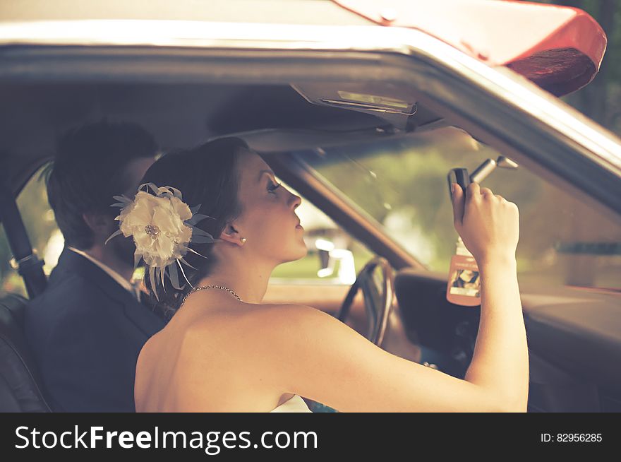 A young wedding couple sitting in a car, the bride looking at a rear mirror inside. A young wedding couple sitting in a car, the bride looking at a rear mirror inside.