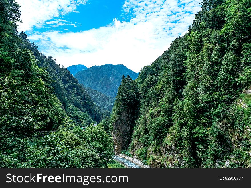 Valley with forest on both steep sides and river on the valley floor, dark distant mountain, blue sky and cloud as background. Valley with forest on both steep sides and river on the valley floor, dark distant mountain, blue sky and cloud as background.