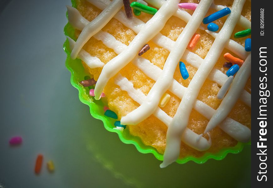 Close up of vanilla cupcake in green wrapper with white frosting and colorful sprinkles. Close up of vanilla cupcake in green wrapper with white frosting and colorful sprinkles.