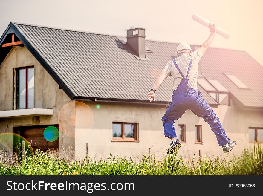 Construction worker or architect jumping for joy holding blueprints outside house on sunny day. Construction worker or architect jumping for joy holding blueprints outside house on sunny day.