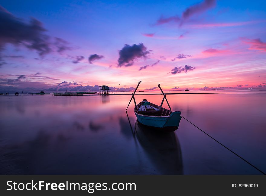 Wooden boat tied to shores in still waters of Vietnam at sunset with purple skies. Wooden boat tied to shores in still waters of Vietnam at sunset with purple skies.