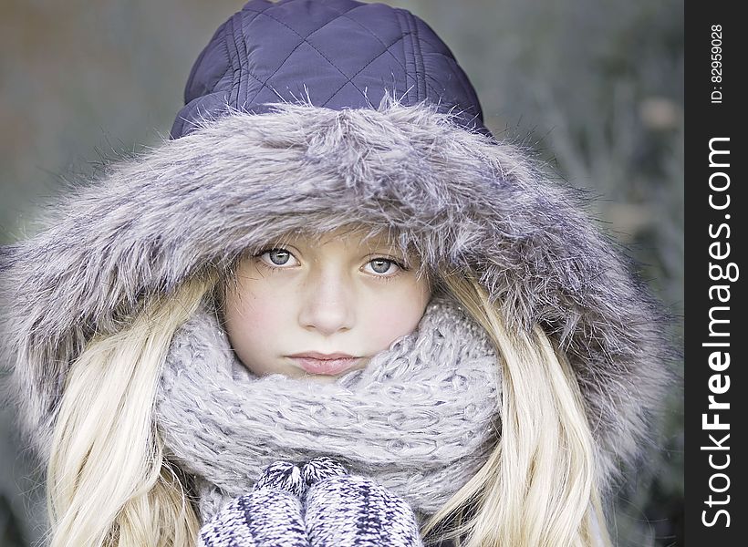 Portrait of blond haired girl in purple winter jacket and knit scarf outdoors.