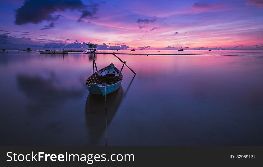 Wooden rowboat tied to shores in still waters at sunset with purple skies. Wooden rowboat tied to shores in still waters at sunset with purple skies.