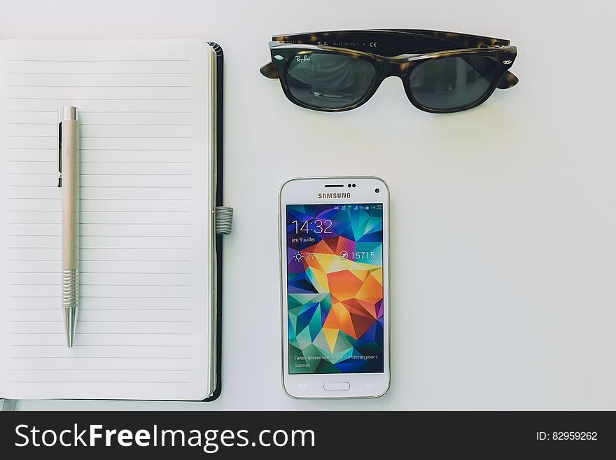 White Samsung Smartphone Beside Sunglasses,pen And White Notebook