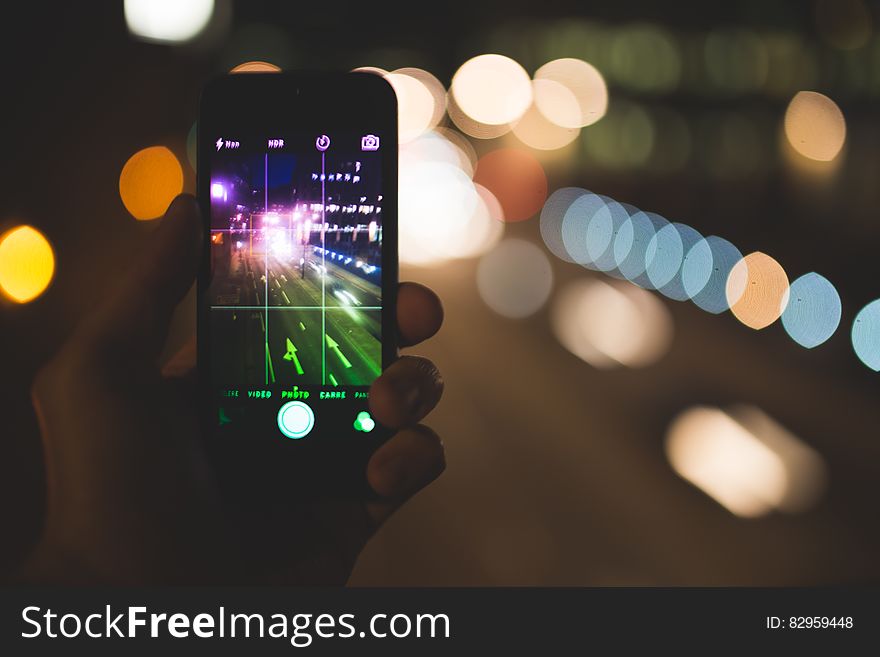 Hand holding smartphone against urban bokeh background.