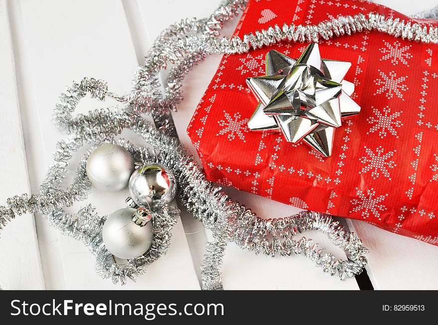 Red and silver wrapping paper on package with bow covered in garland and balls on white. Red and silver wrapping paper on package with bow covered in garland and balls on white.