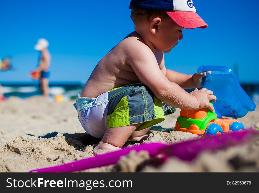 Side view of young boy playing with toys on sandy beach with blue sky and sea background. Side view of young boy playing with toys on sandy beach with blue sky and sea background.