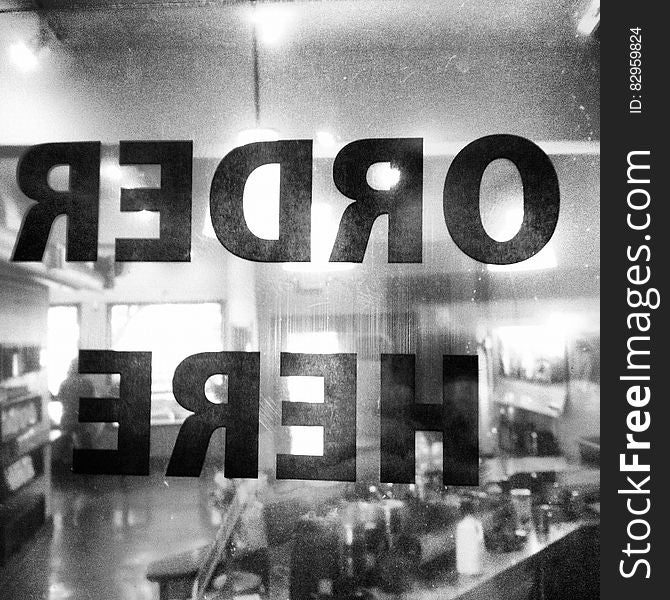 A view through a cafeteria window in black and white with the text "order here".